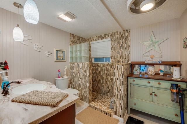 bathroom with a textured ceiling, tile patterned floors, vanity, toilet, and tiled shower