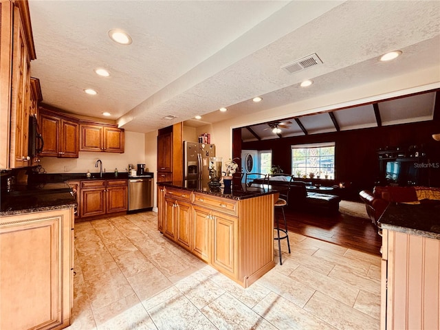 kitchen featuring a kitchen bar, a textured ceiling, lofted ceiling with beams, and stainless steel appliances