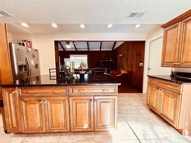 kitchen featuring a textured ceiling, dark stone countertops, wood walls, and stainless steel refrigerator with ice dispenser