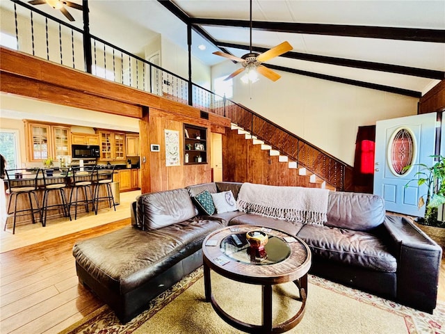 living room featuring beam ceiling, light hardwood / wood-style floors, high vaulted ceiling, and ceiling fan