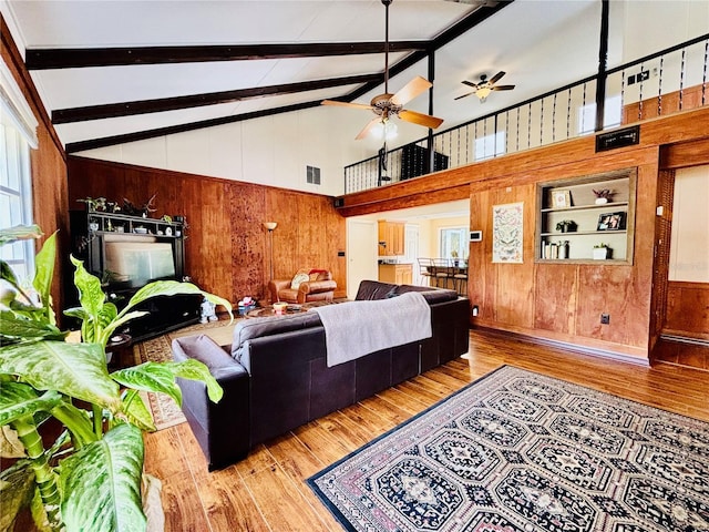 living room with beam ceiling, ceiling fan, high vaulted ceiling, wooden walls, and hardwood / wood-style flooring