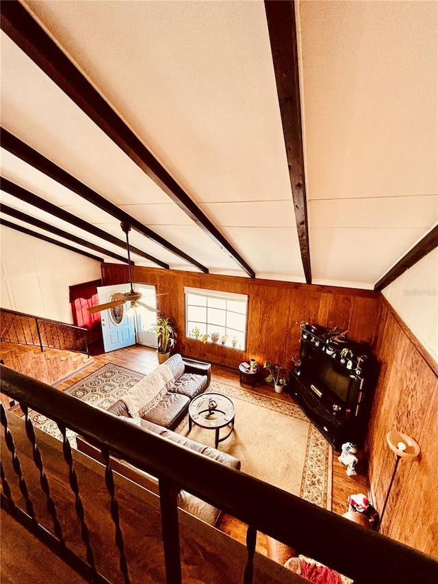 unfurnished living room featuring wood walls, ceiling fan, and lofted ceiling with beams