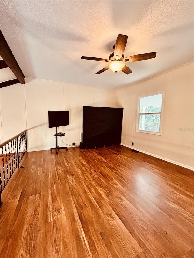 empty room with hardwood / wood-style floors, vaulted ceiling with beams, ceiling fan, and a textured ceiling