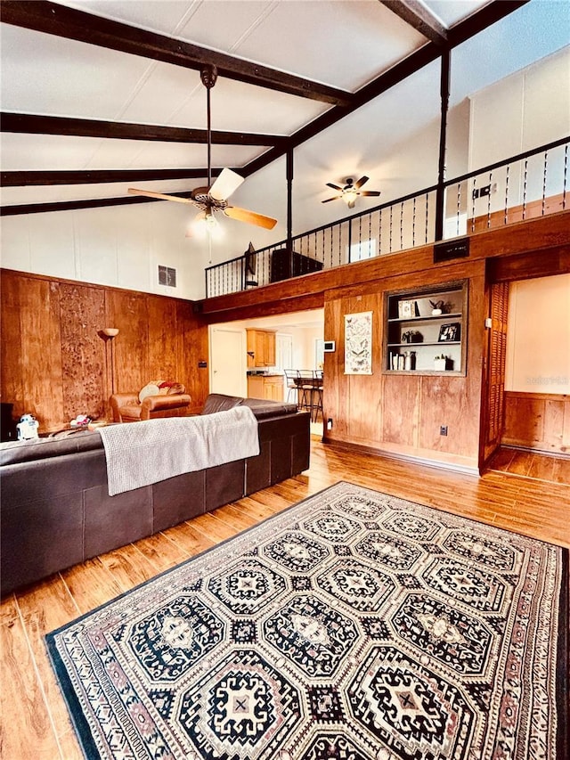 living room with wood walls, ceiling fan, beam ceiling, and wood-type flooring