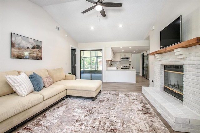 living room featuring a brick fireplace, a textured ceiling, ceiling fan, high vaulted ceiling, and light hardwood / wood-style flooring