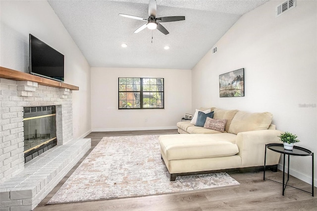 living room featuring a textured ceiling, vaulted ceiling, ceiling fan, hardwood / wood-style flooring, and a fireplace