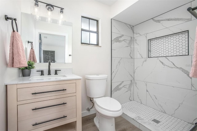 bathroom with tiled shower, toilet, vanity, and hardwood / wood-style flooring