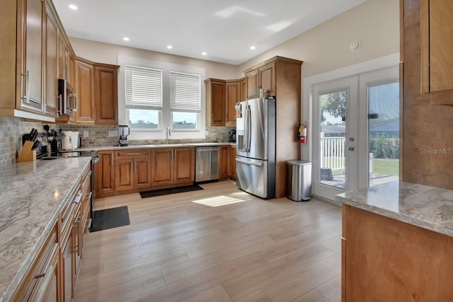 kitchen featuring appliances with stainless steel finishes, light hardwood / wood-style flooring, plenty of natural light, and light stone counters