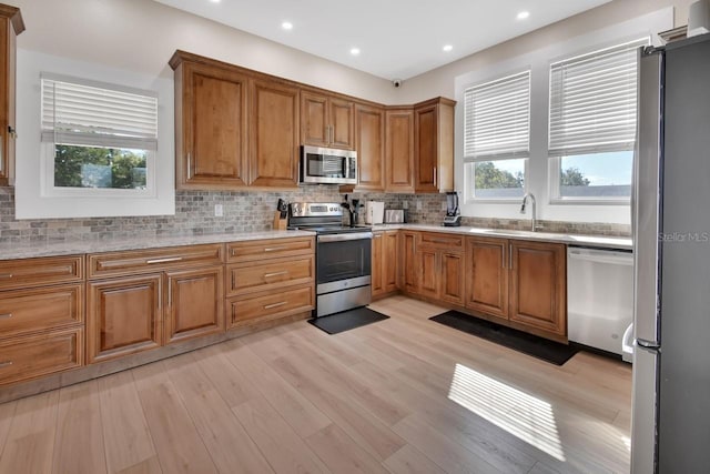 kitchen featuring decorative backsplash, appliances with stainless steel finishes, light stone countertops, sink, and light hardwood / wood-style floors