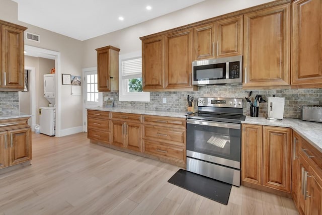 kitchen featuring backsplash, stacked washer and dryer, light hardwood / wood-style flooring, and appliances with stainless steel finishes