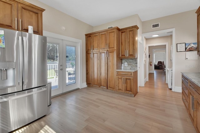 kitchen with decorative backsplash, stainless steel fridge, light wood-type flooring, french doors, and light stone counters