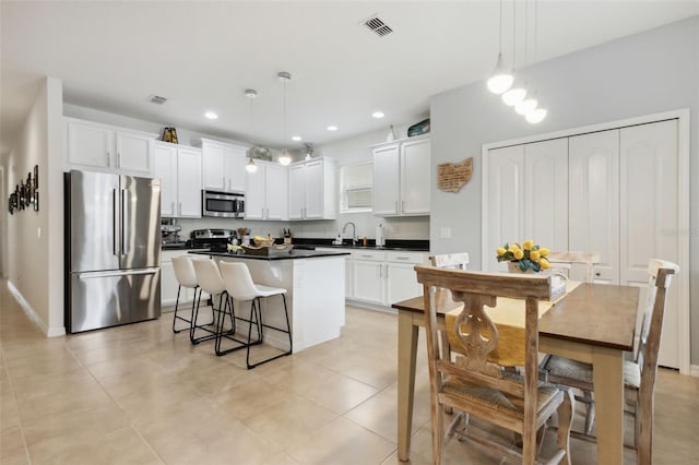 kitchen with decorative light fixtures, a center island, stainless steel appliances, and white cabinetry