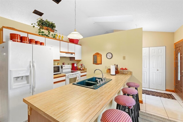 kitchen featuring white appliances, kitchen peninsula, lofted ceiling with skylight, sink, and decorative light fixtures