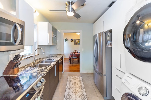 kitchen with appliances with stainless steel finishes, sink, stacked washer and dryer, white cabinetry, and light tile patterned flooring