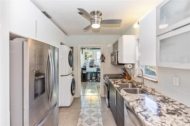 kitchen featuring sink, light stone countertops, white cabinetry, stacked washer / dryer, and stainless steel appliances