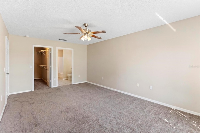 unfurnished bedroom with a walk in closet, a textured ceiling, light colored carpet, ceiling fan, and a closet