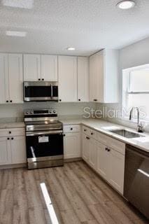 kitchen with white cabinets, sink, appliances with stainless steel finishes, and light hardwood / wood-style flooring