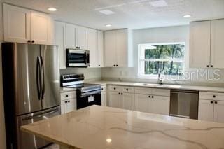 kitchen featuring sink, stainless steel appliances, white cabinetry, and light stone counters