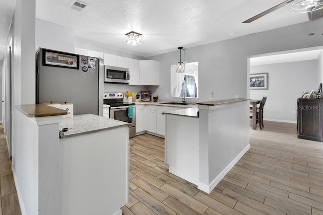 kitchen featuring sink, stainless steel appliances, pendant lighting, white cabinets, and light wood-type flooring