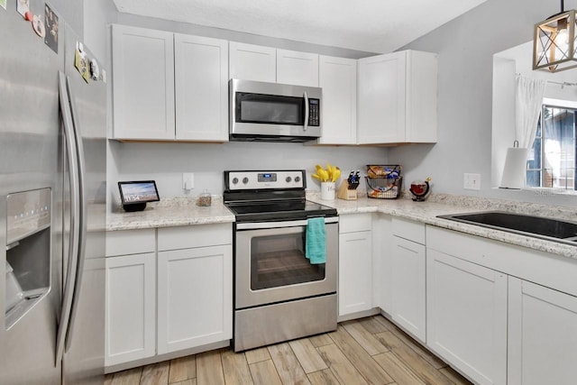 kitchen with white cabinets, light hardwood / wood-style floors, stainless steel appliances, and hanging light fixtures