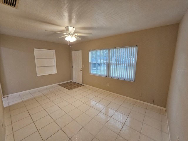 spare room with ceiling fan, built in features, light tile patterned floors, and a textured ceiling