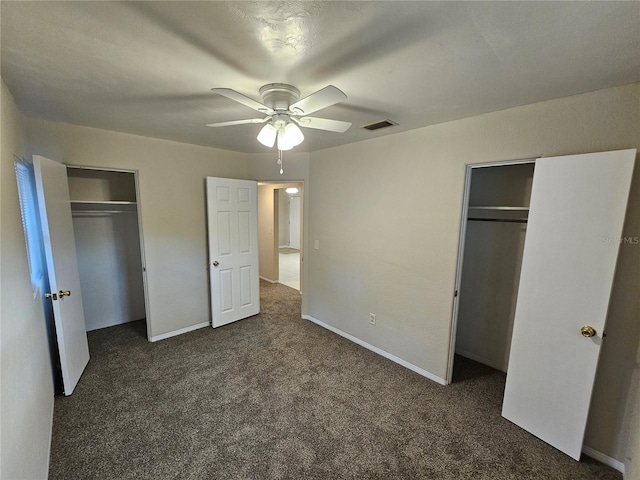 unfurnished bedroom with ceiling fan, dark carpet, and two closets