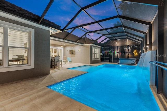 pool at dusk featuring glass enclosure, a patio area, and a jacuzzi