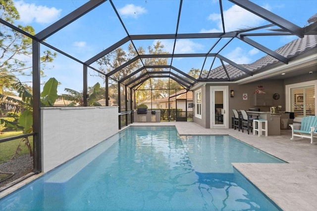 view of pool featuring an outdoor kitchen, a patio area, a bar, and glass enclosure