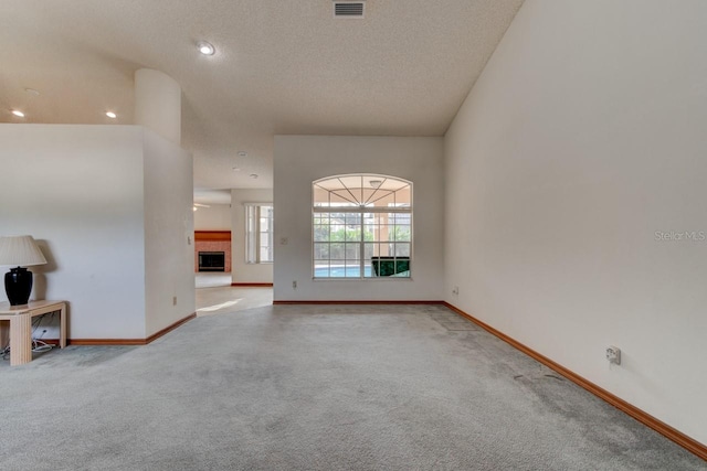 unfurnished living room featuring a tile fireplace, light colored carpet, and a textured ceiling