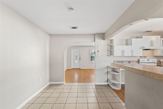 kitchen featuring tile counters, white cabinets, white range, and light wood-type flooring