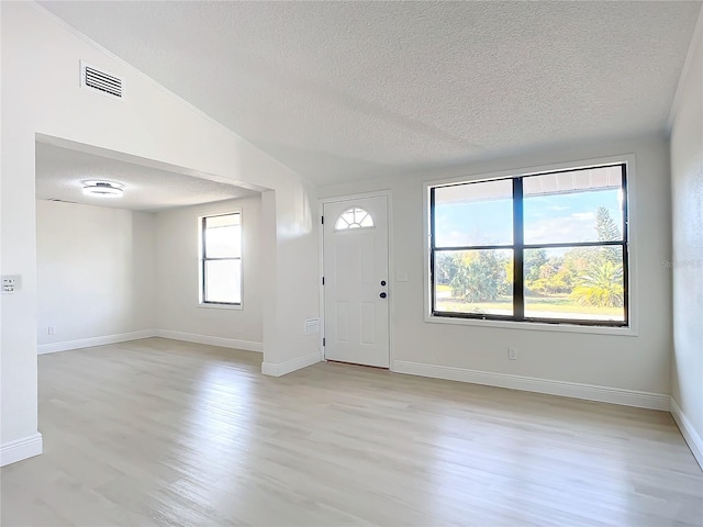 foyer with lofted ceiling, a textured ceiling, and light wood-type flooring