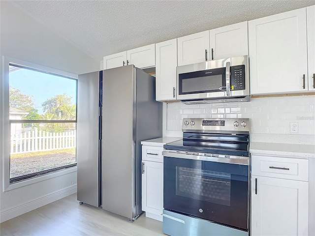 kitchen with white cabinets, light hardwood / wood-style floors, backsplash, and appliances with stainless steel finishes