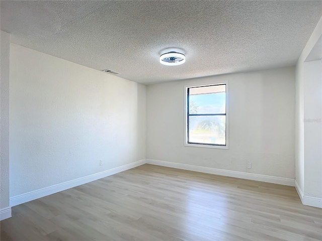 spare room with a textured ceiling and light hardwood / wood-style flooring