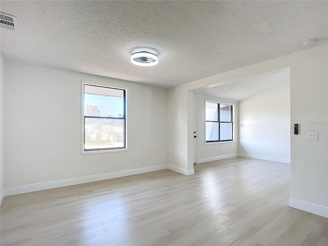 empty room with a healthy amount of sunlight, light wood-type flooring, and a textured ceiling