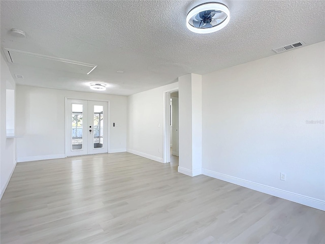 empty room with french doors, a textured ceiling, and light wood-type flooring