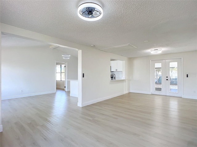 unfurnished living room with a textured ceiling, plenty of natural light, french doors, and light hardwood / wood-style flooring