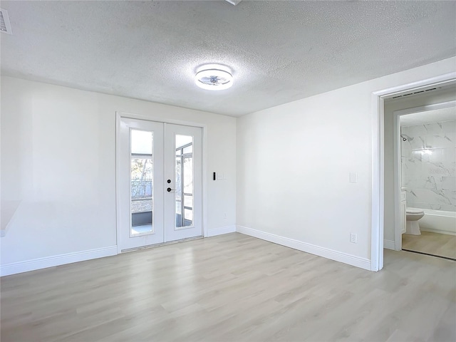 unfurnished room with light hardwood / wood-style floors, a textured ceiling, and french doors