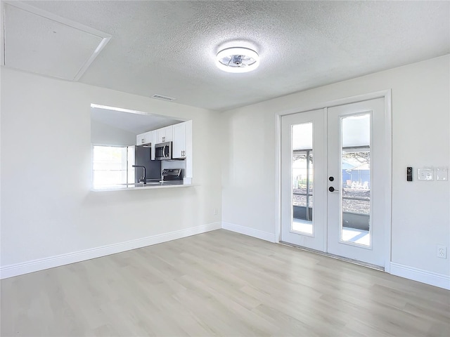 empty room featuring french doors, light wood-type flooring, and a healthy amount of sunlight