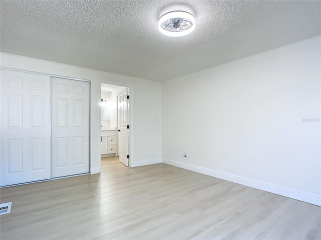 unfurnished bedroom with light wood-type flooring, a textured ceiling, connected bathroom, and a closet