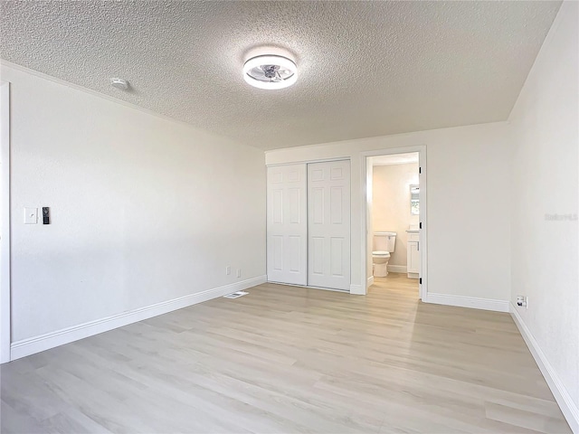 unfurnished bedroom with a textured ceiling, a closet, light hardwood / wood-style flooring, and ensuite bath