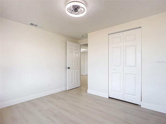 unfurnished bedroom with light wood-type flooring, a textured ceiling, and a closet