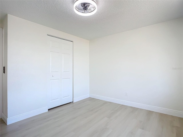 unfurnished bedroom with a textured ceiling, light wood-type flooring, and a closet