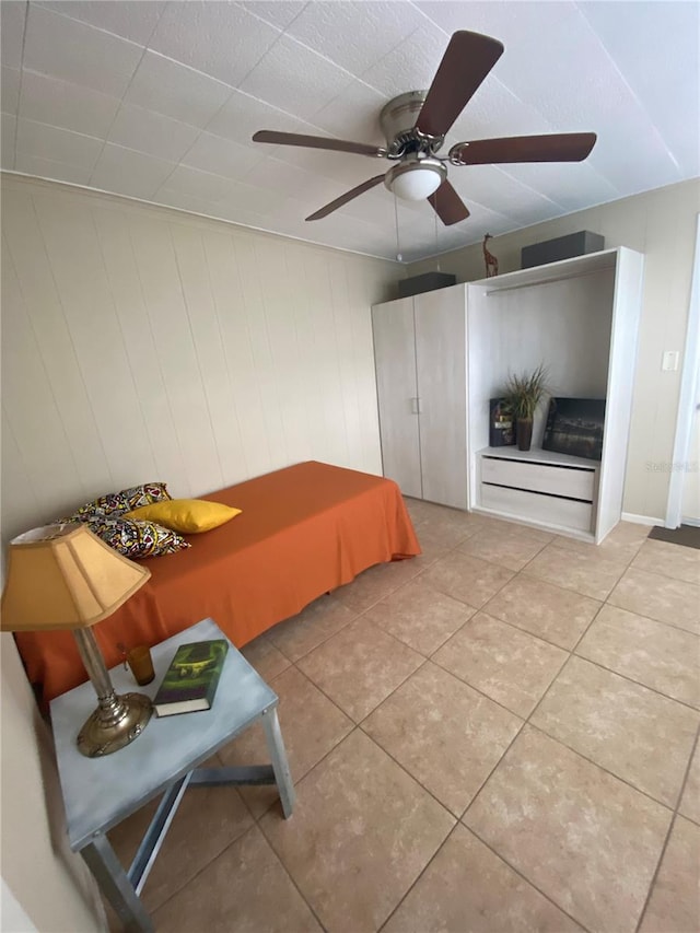 bedroom featuring light tile patterned floors, ceiling fan, and wood walls