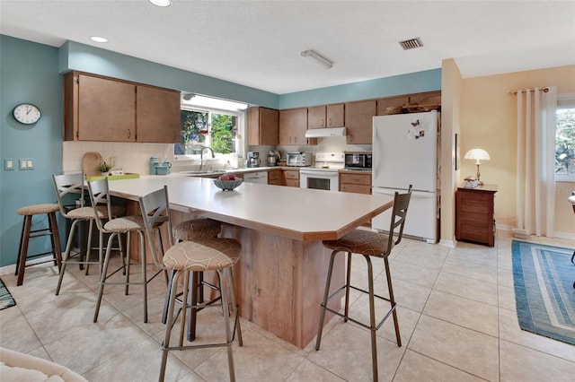 kitchen with kitchen peninsula, a kitchen breakfast bar, white appliances, and light tile patterned floors