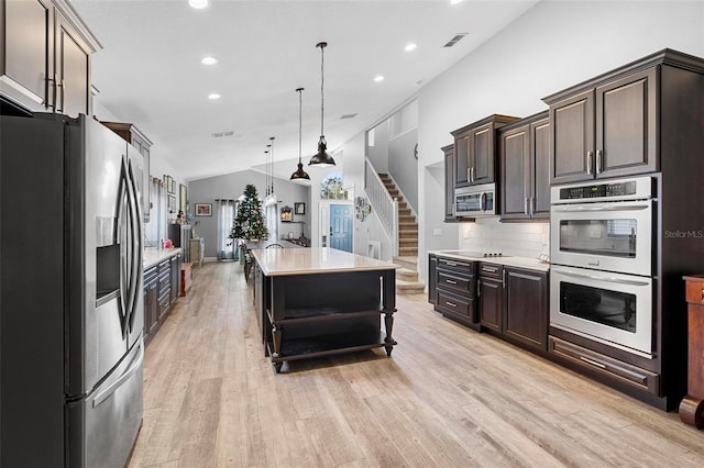 kitchen with appliances with stainless steel finishes, backsplash, dark brown cabinetry, decorative light fixtures, and a kitchen island