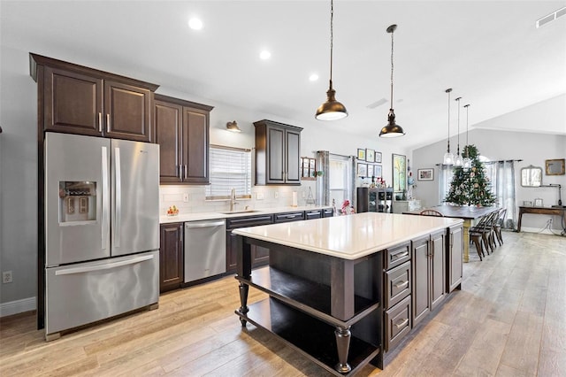 kitchen featuring hanging light fixtures, backsplash, lofted ceiling, a kitchen island, and appliances with stainless steel finishes