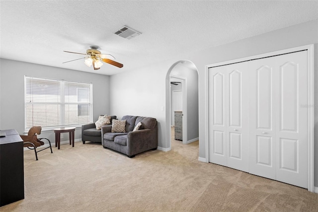 living room featuring a textured ceiling, ceiling fan, and light carpet