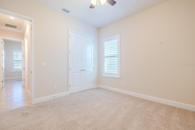 unfurnished bedroom featuring ceiling fan, a closet, light colored carpet, and ornamental molding