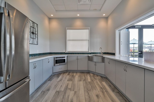 kitchen featuring light wood-type flooring, gray cabinets, stainless steel refrigerator, and sink