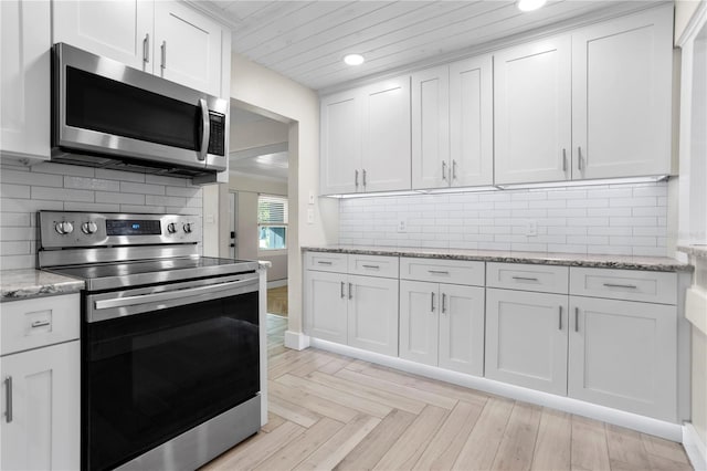 kitchen with white cabinetry, light stone counters, backsplash, light parquet flooring, and appliances with stainless steel finishes